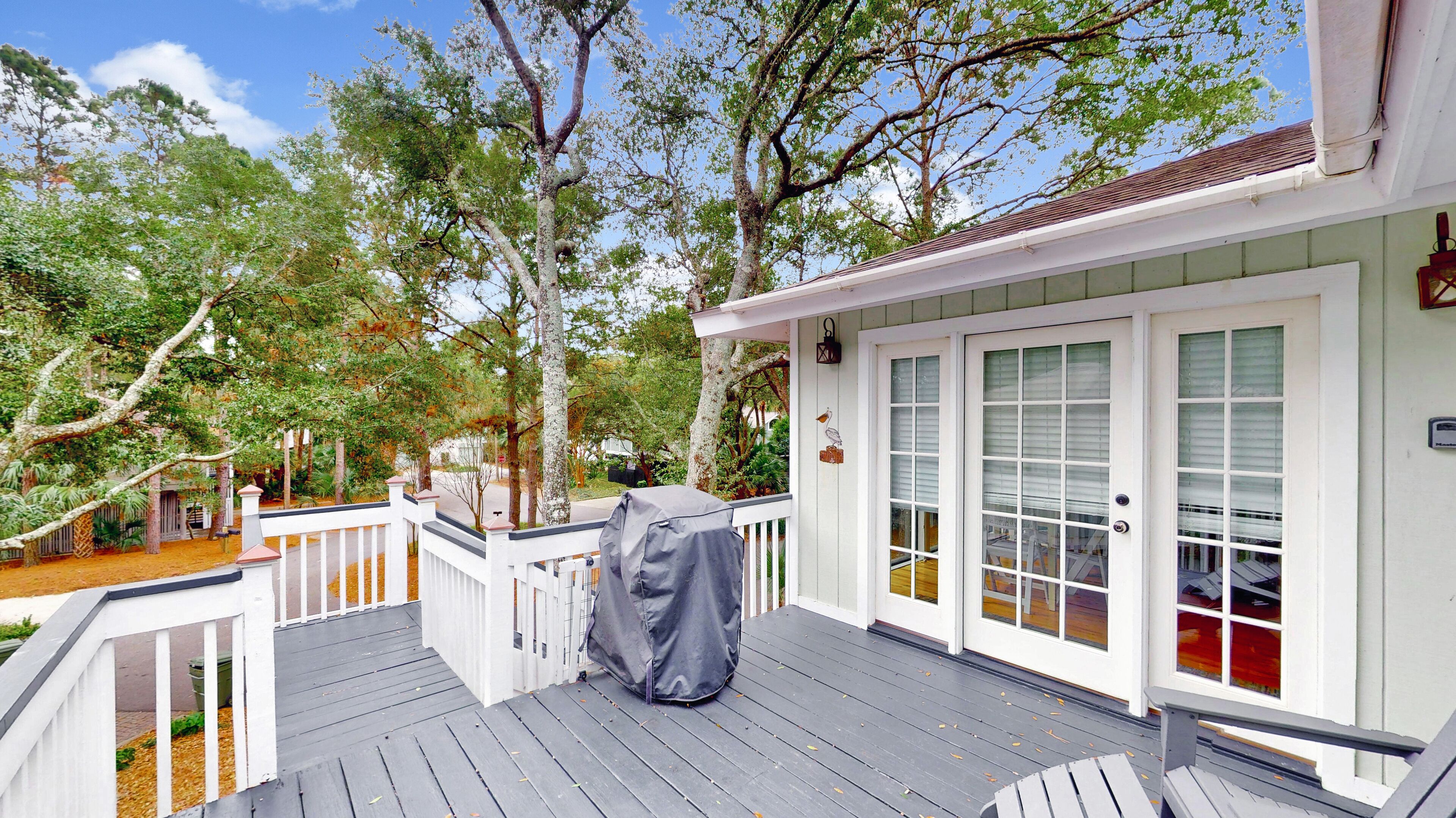A covered deck with a grill, white railings, and a view of a house with a covered porch and a bird decoration.