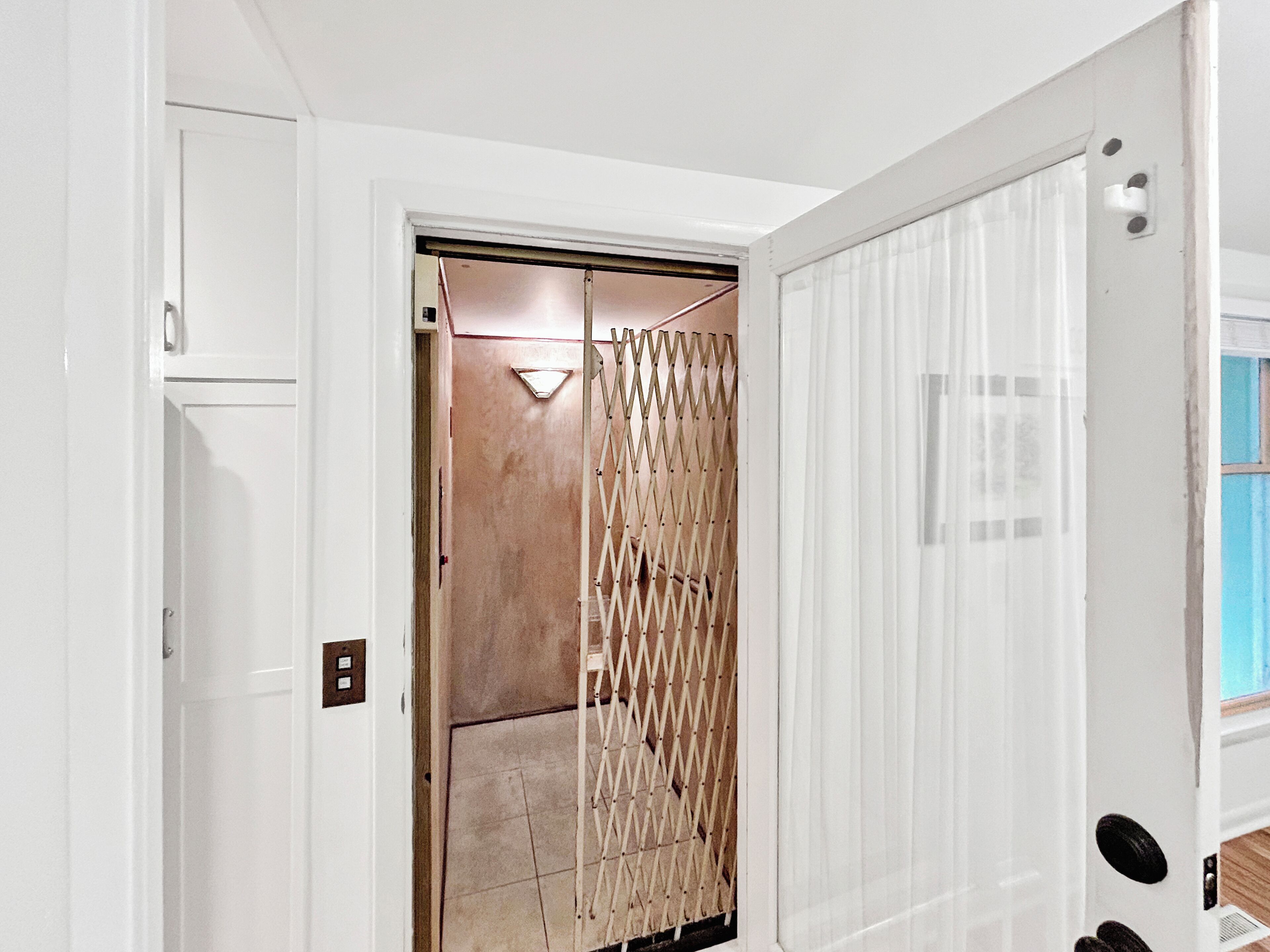 Een kamer met een witte deur, een beige muur en een raam met jaloezieën.