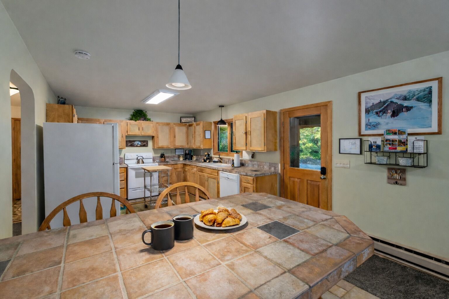 A kitchen with wooden cabinets, a tiled island, and a dining area with chairs.