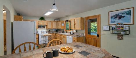 A kitchen with wooden cabinets, a tiled island, and a dining area with chairs.