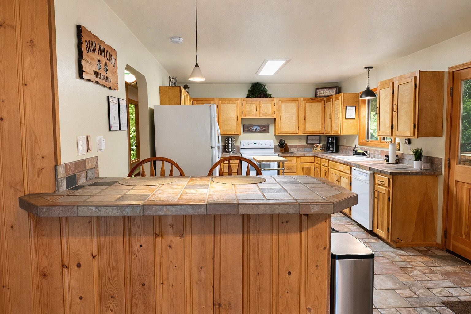 Una cocina con armarios de madera, una isla central con sillas, un refrigerador, una estufa y un fregadero.