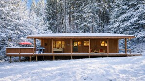 Eine Holzhütte mit Veranda und Sitzgelegenheit, umgeben von schneebedeckten Bäumen.