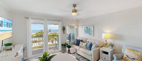A living room with a TV, a sofa, a coffee table, and a view of the beach.