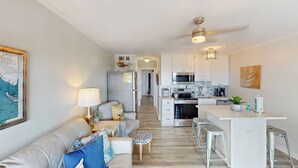 Eine moderne Küche mit Mikrowelle, Herd und Spüle. Es gibt einen Essbereich mit einer Couch und einer Lampe. Die Küche verfügt über eine weiße Arbeitsplatte und Edelstahlgeräte.