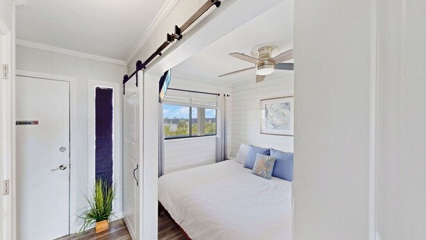 Un dormitorio con cama, ventilador de techo, ventana con vistas y puerta con letrero de 'no fumar'.