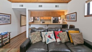 A living room with a leather couch, a kitchen in the background, and a loft area above.