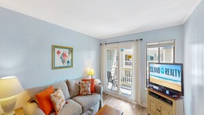 A living room with a sofa, a TV displaying 'ISLAND REALTY,' and a balcony with a view.