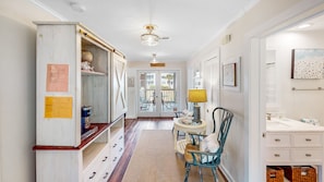 A hallway with a wooden cabinet, a dining area with a table and chairs, and a bathroom with a sink and mirror.