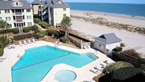 Ein Schwimmbecken mit Liegestühlen, ein Strand und ein Gebäude mit Balkonen.