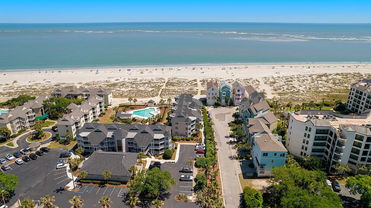 A coastal hotel with multiple buildings, a parking lot, and a beach view.