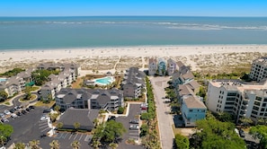 A coastal hotel with multiple buildings, a parking lot, and a beach view.