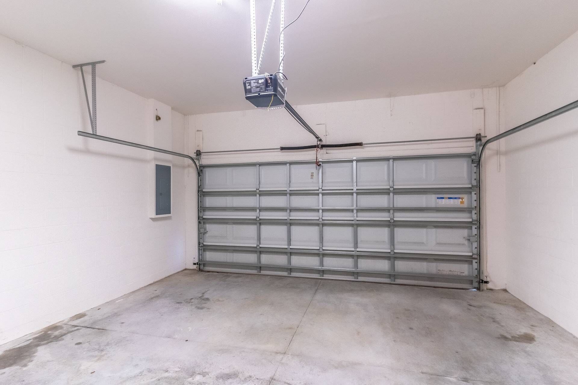 A garage with a closed metal door, concrete floor, and a ceiling-mounted projector.