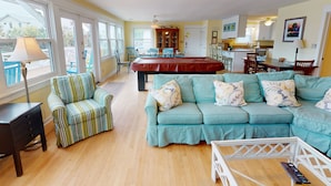 A spacious living room with a pool table, a teal sofa, and a dining area with wooden chairs. - Pet friendly home with pool, billiard table; across the street from beach. (Isle of Palms)