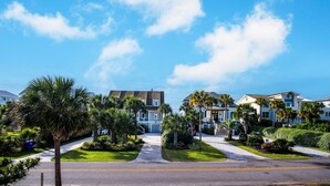 A residential street with houses, palm trees, and a clear blue sky. - Pet friendly home with pool, billiard table; across the street from beach. (Isle of Palms)
