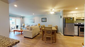 Un salon avec un canapé, une table à manger et des chaises, une cuisine équipée d’un réfrigérateur et d’une cuisinière, et un ventilateur de plafond.