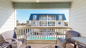 Un balcon avec des fauteuils en osier et une table, donnant sur une piscine et un immeuble doté de balcons.
