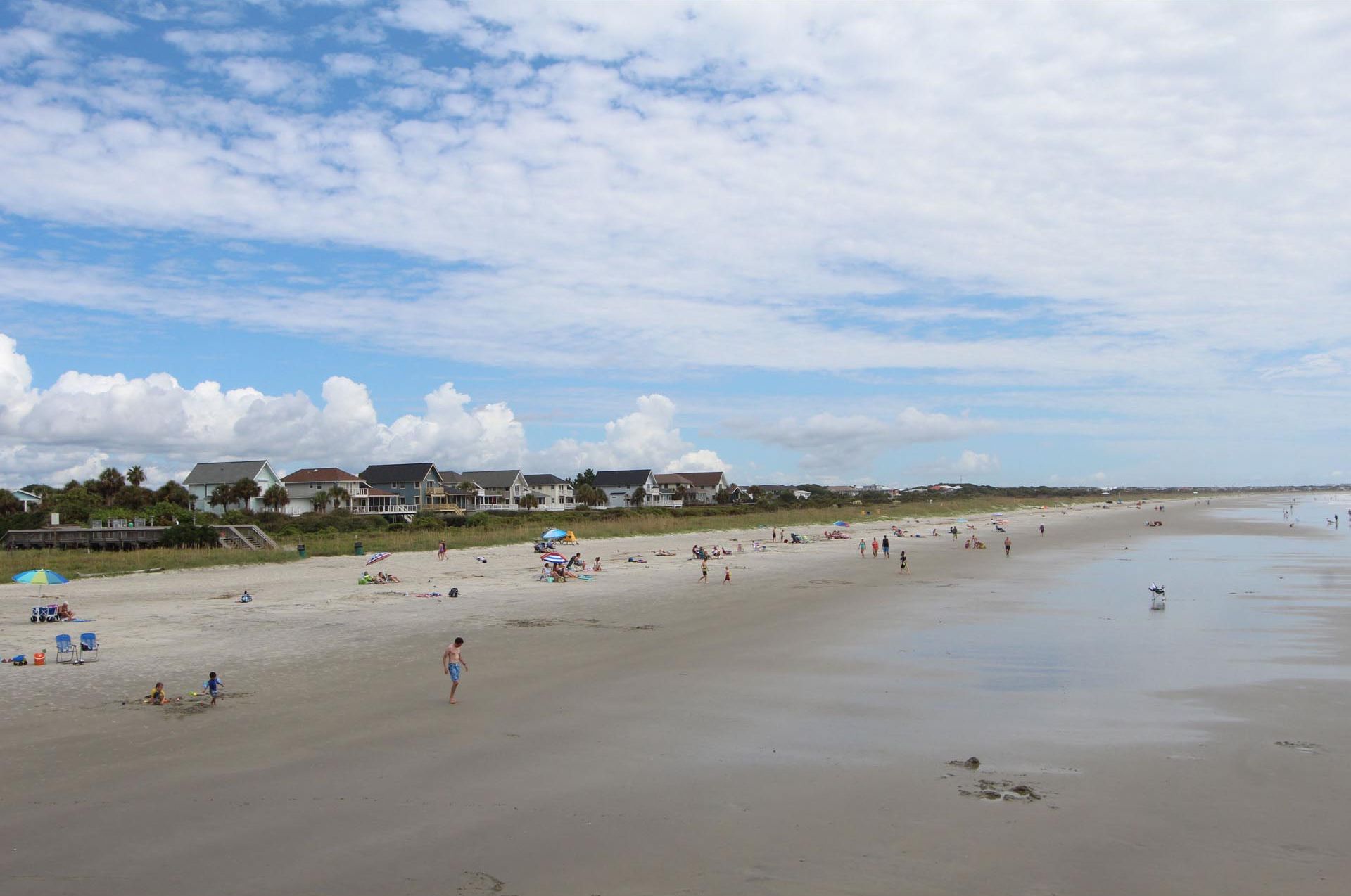 A beach with houses in the background and people on the sand.