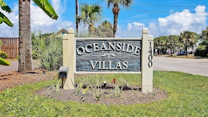 Une enseigne indiquant l’emplacement d’Oceanside Villas, entourée d’une végétation tropicale et sous un ciel dégagé.