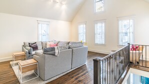 A spacious living room with a gray sofa, wooden side tables, and a staircase with a railing.