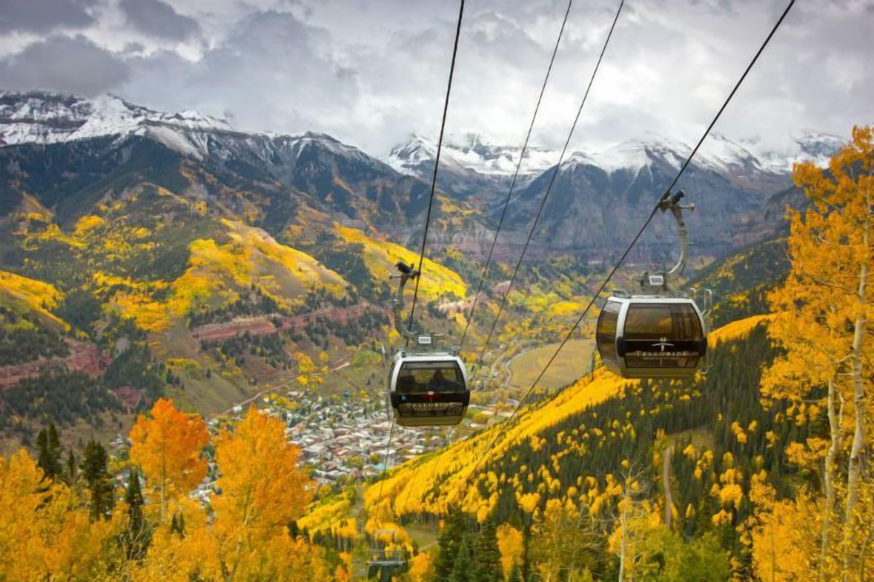 A cable car system in a mountainous area with autumn foliage and snow-capped peaks in the background.