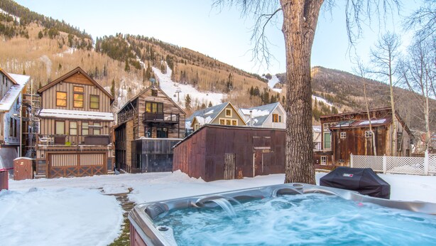 A hot tub in a snowy outdoor area with wooden cabins and a mountain backdrop.