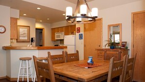 A wooden dining table with six chairs, a kitchen area with wooden cabinets, a microwave, and a refrigerator. - Affordable Purgatory Ski in/Ski Out Condo in the Main Plaza (Durango)