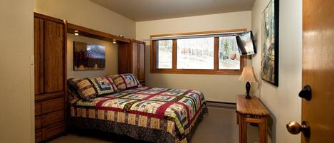 Une chambre avec un grand lit, une fenêtre, une télévision et une porte.