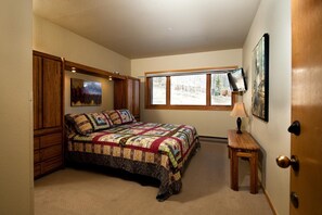 Un dormitorio con una cama grande, una ventana, un televisor y una puerta.
