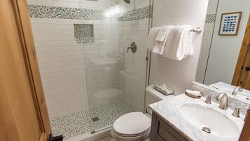 A bathroom with a glass-enclosed shower, a toilet, and a vanity with a sink and mirror.