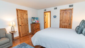 Un dormitorio con una cama grande, un armario de madera, un tocador, una silla y un televisor sobre un mueble de madera.