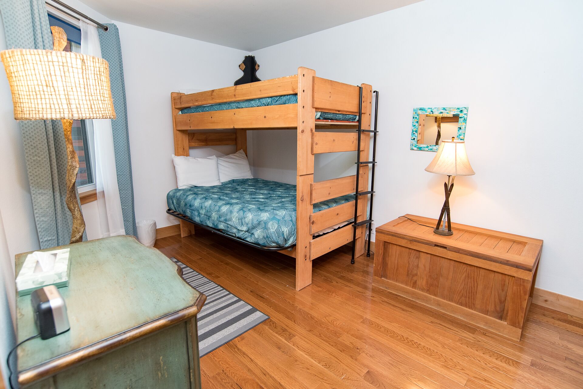 A bunk bed with a ladder, a bedside table, a lamp, and a mirror on the wall.