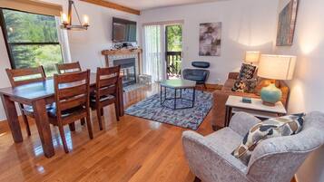 A living room with a wooden dining table, chairs, a sofa, a TV, and a fireplace.