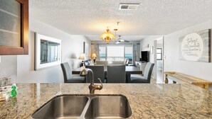 A modern kitchen with a double sink, granite countertops, and a dining area with a chandelier. - Beachfront - Ocean Views - Beach Place #108 (Madeira Beach)