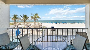 A balcony with a view of a beach, palm trees, and a clear sky. - Beachfront - Ocean Views - Beach Place #108 (Madeira Beach)