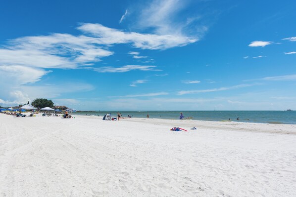 A beach with white sand, clear blue sky, and calm sea.