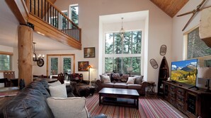 Ein geräumiges Wohnzimmer mit hohen Decken, großen Fenstern, einer Holztreppe und einer gemütlichen Sitzecke mit Kamin.