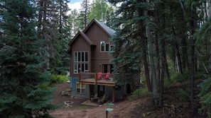 Une cabane à deux étages dotée d’une terrasse, entourée d’une forêt dense.
