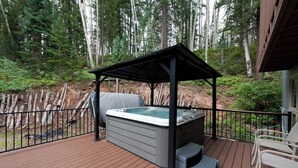 Ein Whirlpool auf einer Holzterrasse mit einer Pergola darüber, umgeben von einem Holzzaun und Bäumen.