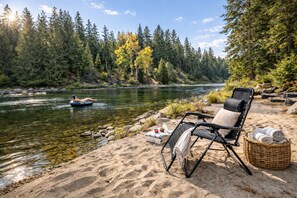 Aussicht auf einen Fluss mit einem Stuhl und einem Korb, ein Floß im Fluss und ein Wald im Hintergrund.