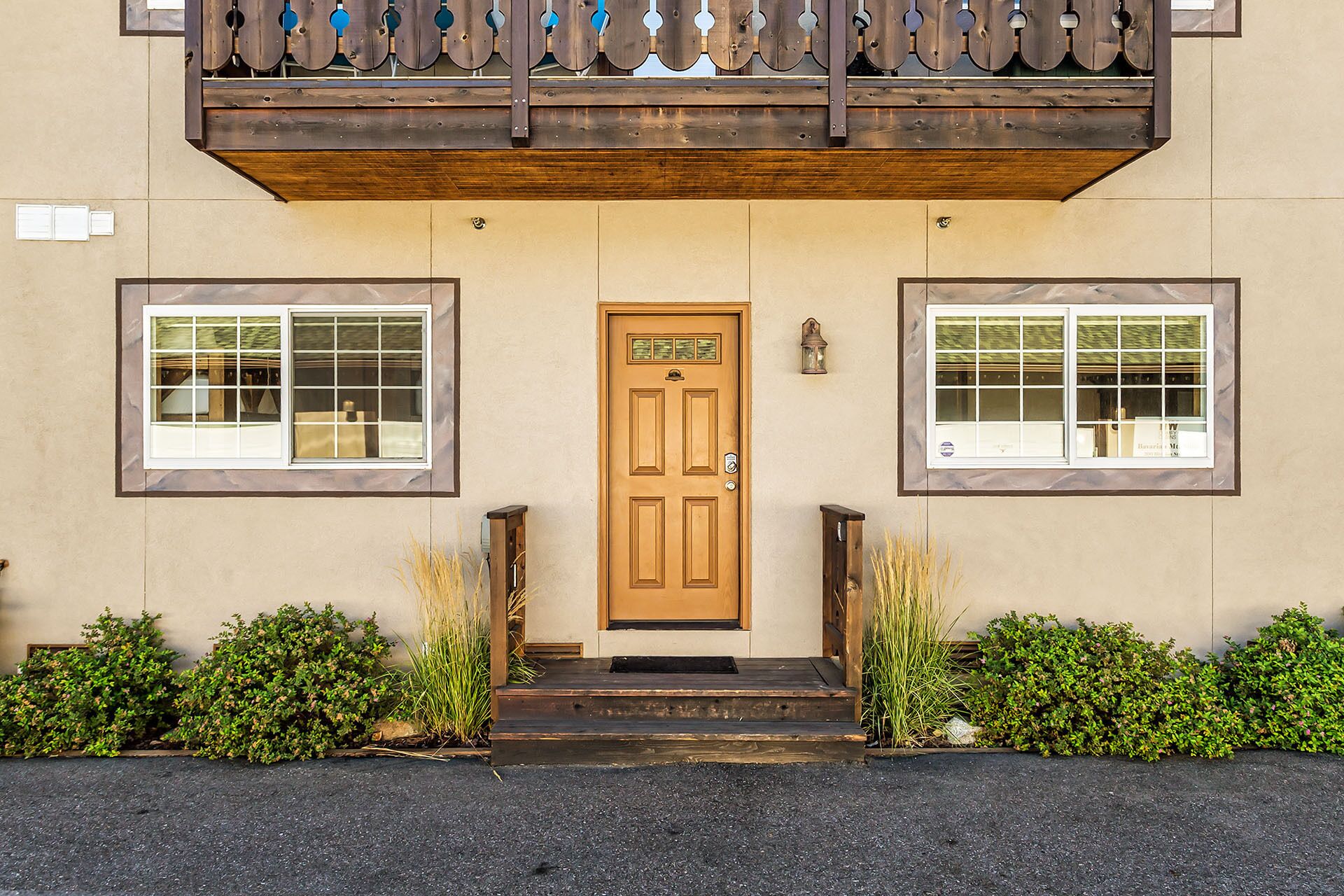 A building with a wooden front door, two windows on either side, and a small porch area with steps leading up to the door.