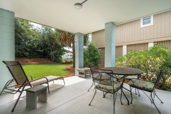 An outdoor patio with a round table and chairs, a bench, and a view of a green lawn and trees.