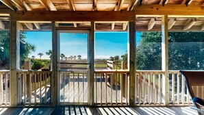 Un espacio al aire libre cubierto, con barandillas de madera y vistas a una playa y palmeras.