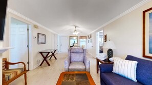A spacious living room with a blue sofa, a wooden coffee table, a patterned armchair, and a dining area with a glass-top table.