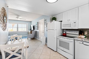 Una cocina moderna con armarios blancos, un refrigerador, un microondas, un horno y una tetera. Cuenta con un comedor con mesa y sillas.