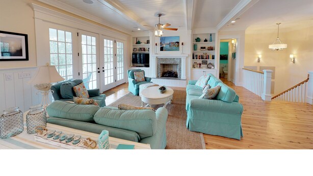 A spacious living room with a fireplace, teal sofas, and a wooden floor. - Beautiful beach home with wrapping porches, private pool, and ocean view peek (Isle of Palms)