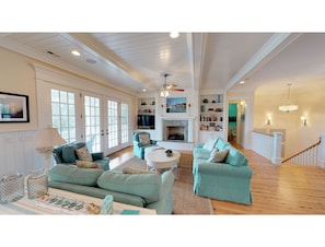 A spacious living room with a fireplace, teal sofas, and a wooden floor. - Beautiful beach home with wrapping porches, private pool, and ocean view peek (Isle of Palms)