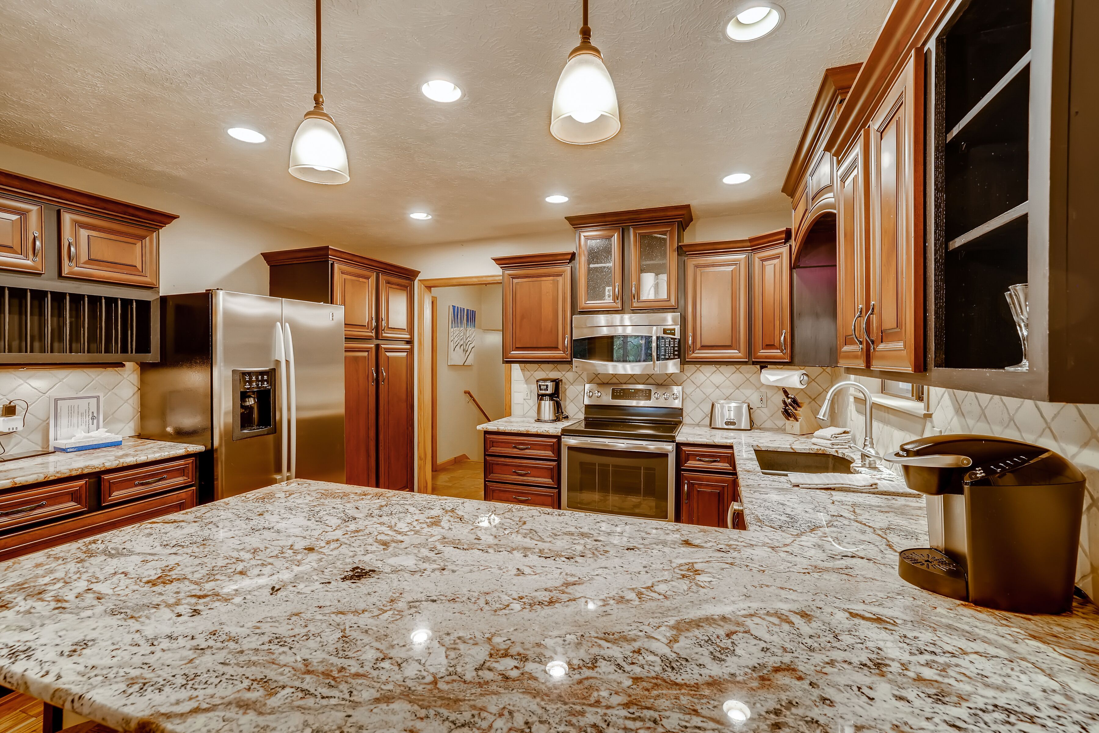 A kitchen with wooden cabinets, stainless steel appliances, and a marble countertop.