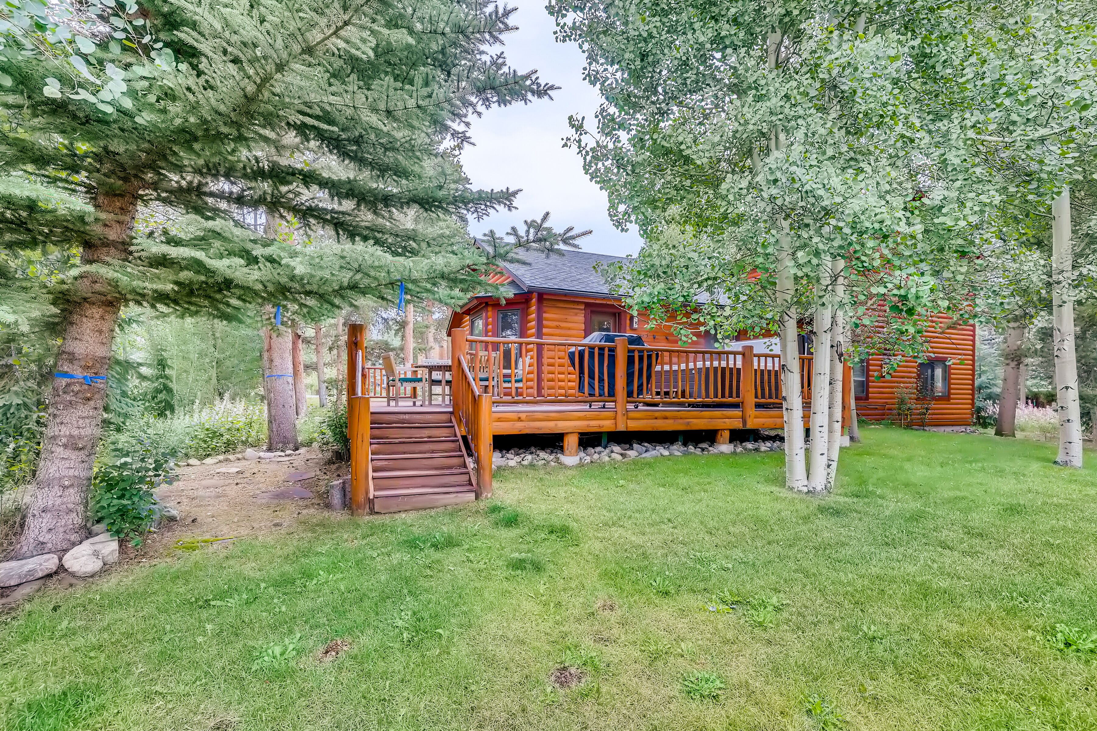 A wooden cabin with a deck, surrounded by trees and a grassy area.