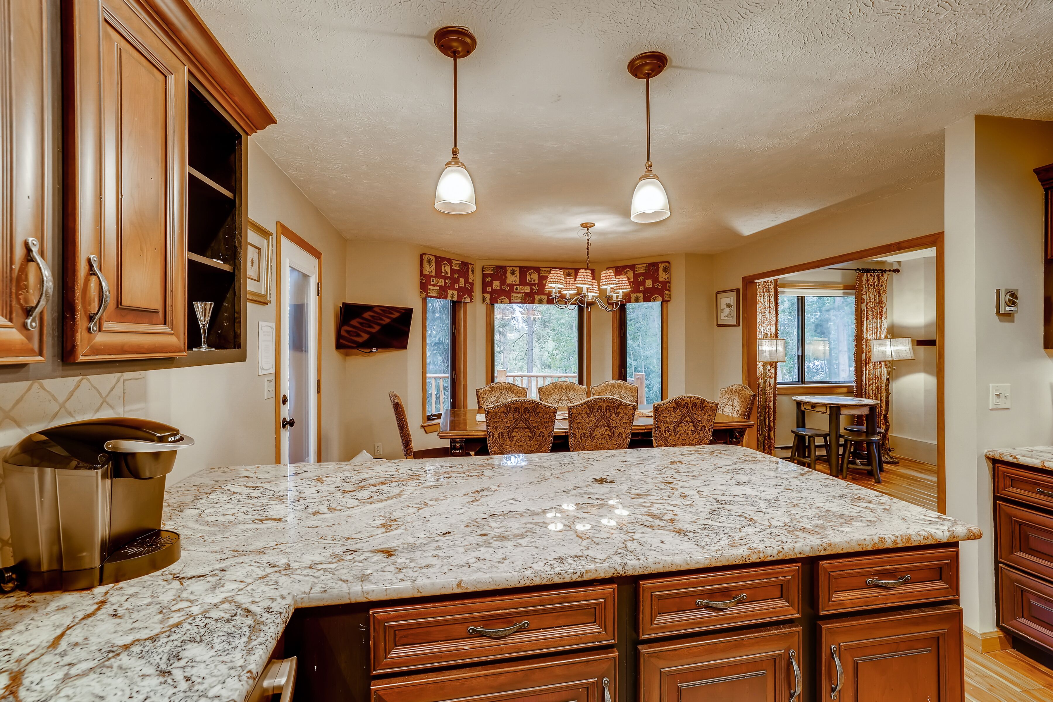 A kitchen with a large marble island, wooden cabinets, and pendant lighting.