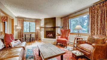 A cozy living room with a fireplace, leather sofas, a wooden coffee table, and patterned curtains.